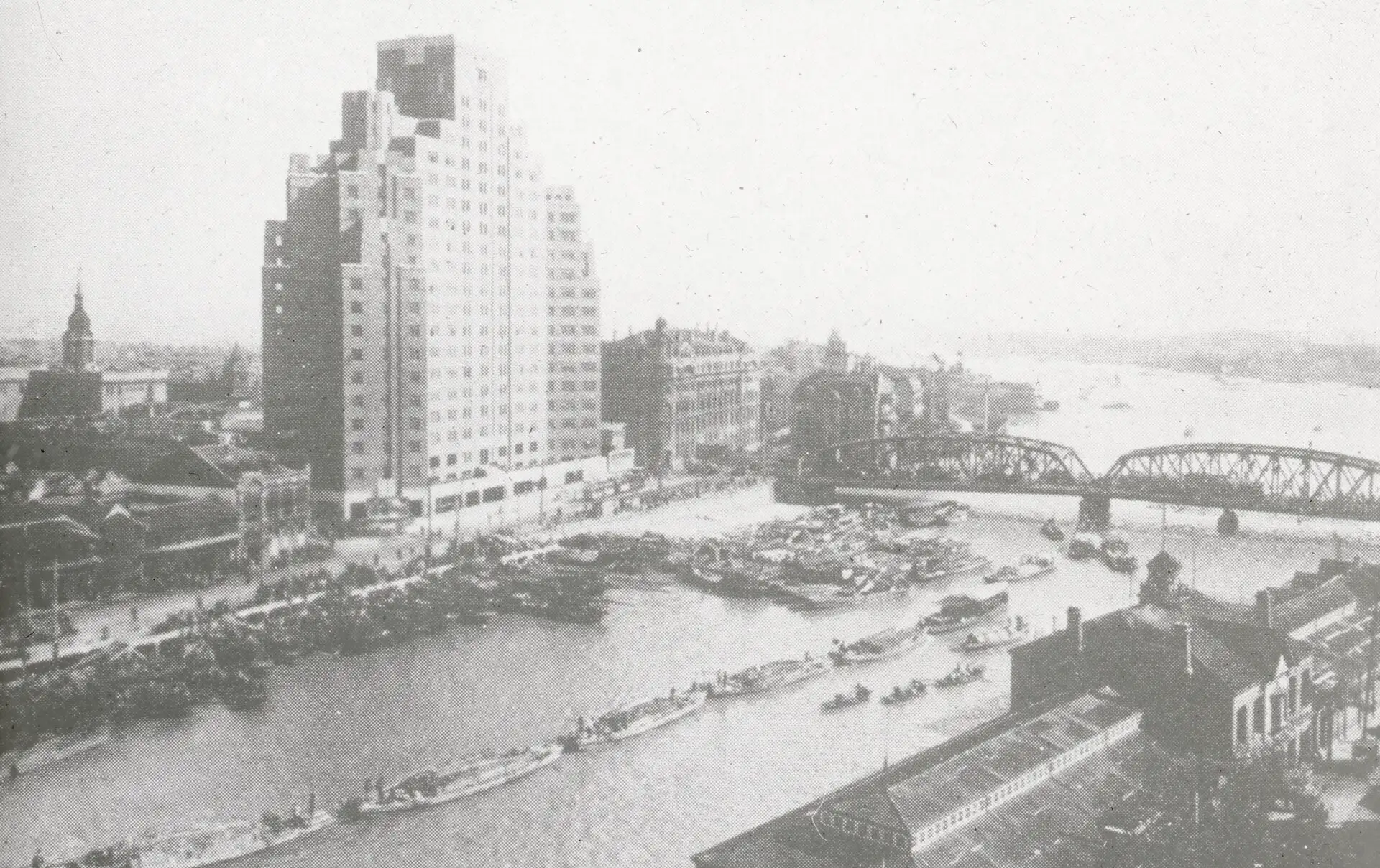 Broadway Mansions, a stepped brick tower, rising above the Garden Bridge and Suzhou Creek, seen from above in an early 20th-century photograph.
