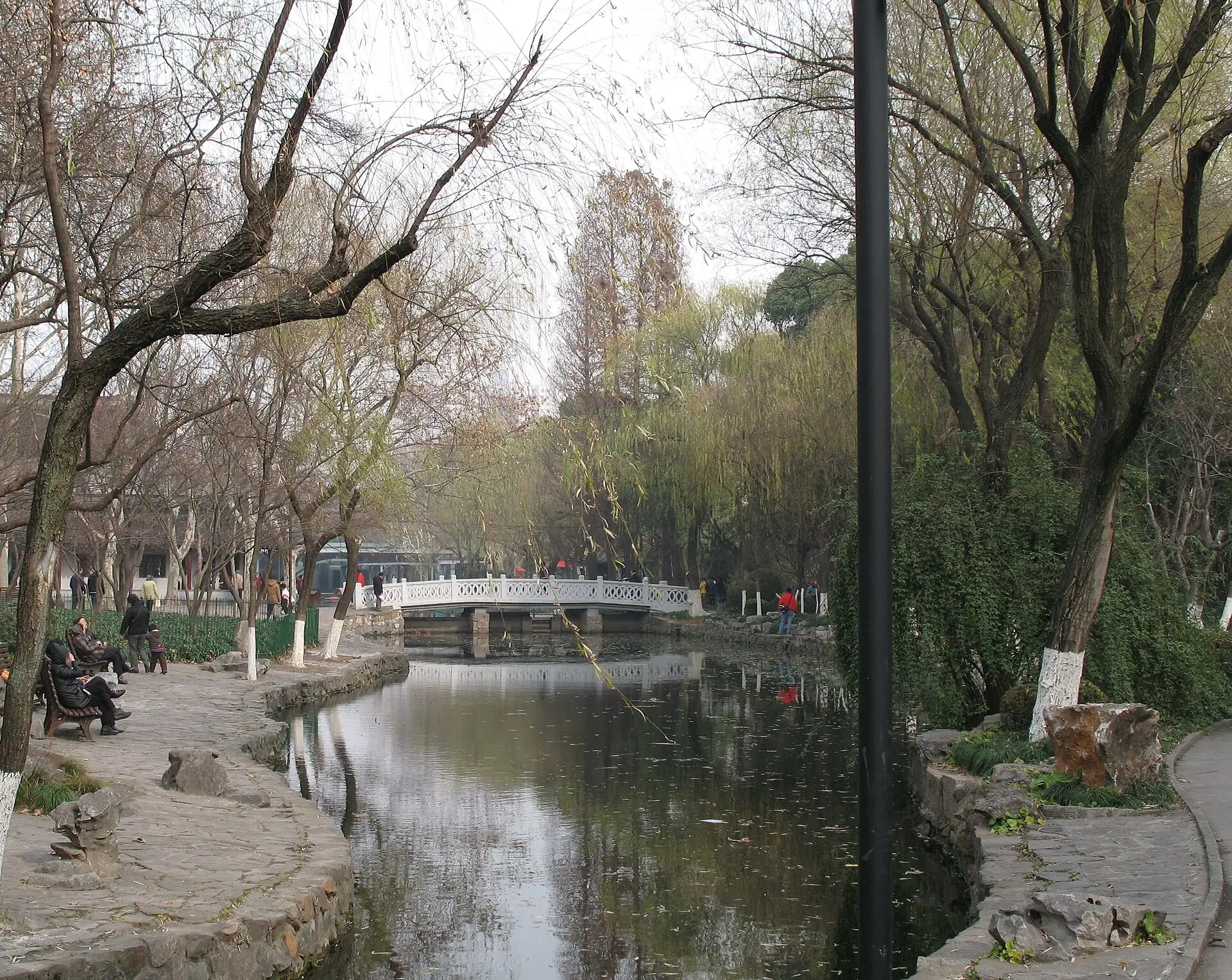 A pond with a stone bridge among trees in Lu Xun Park in winter.