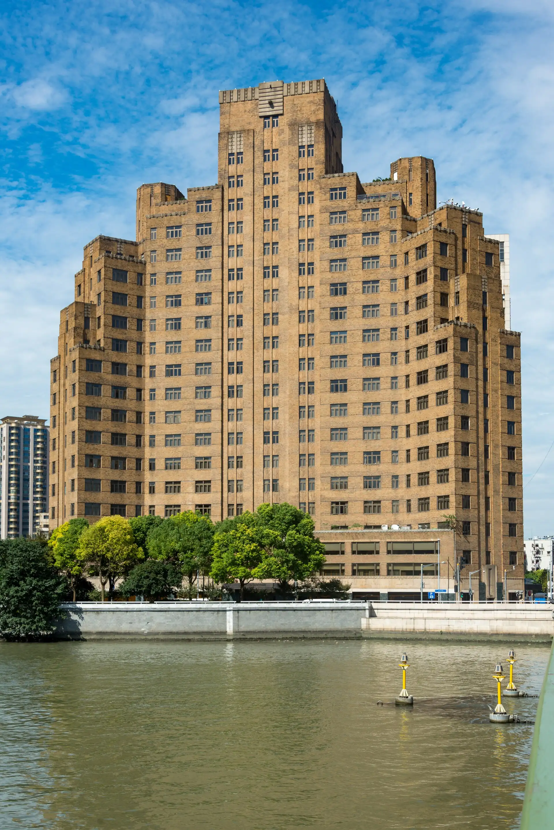 Broadway Mansions, a stepped brown-brick tower, rising beside Suzhou Creek under a blue sky.