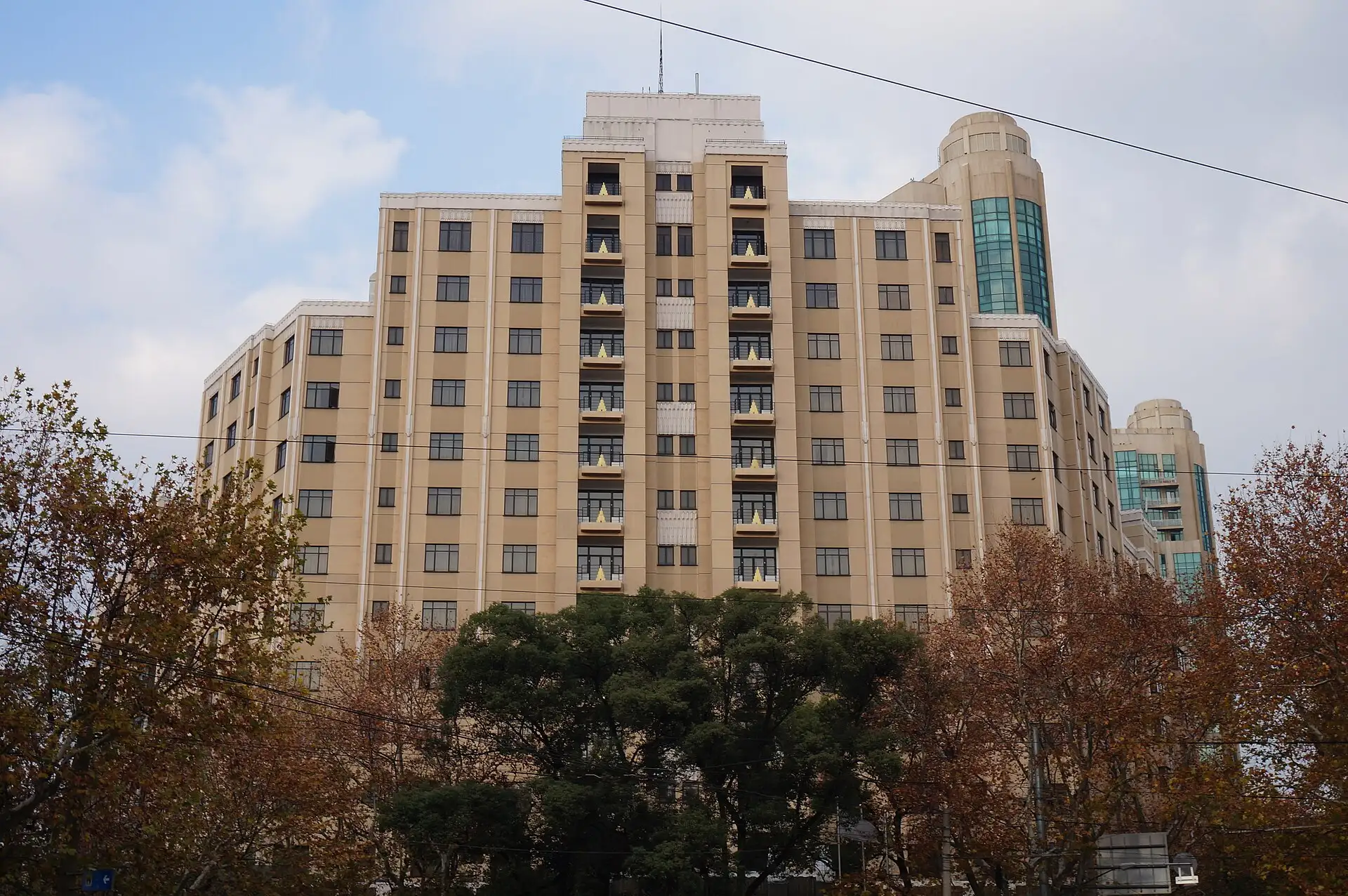 The Hengshan Picardie Hotel, a tall cream apartment block, above trees.