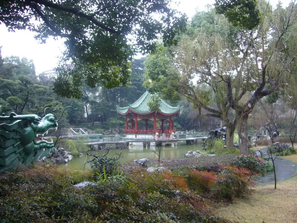 A red pavilion among trees beside a pond in Dingxiang Garden.