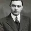 Black-and-white studio portrait of a young clean-shaven man in a tweed jacket and dark tie.