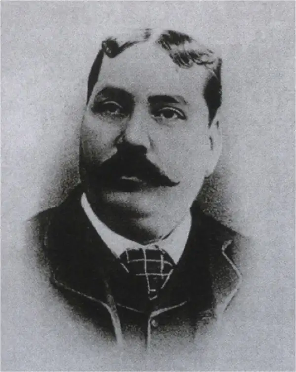Black-and-white oval portrait of a heavy-set man with a dark moustache, wearing a checked tie and dark jacket.