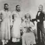 Black-and-white group photograph of an elderly bearded man in a turban, seated, with three men standing beside him.
