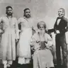 Black-and-white group photograph of an elderly bearded man in a turban, seated, with three men standing beside him.