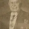 Faded newspaper-style photograph of an elderly man with a white moustache in evening dress with a sash and medals.