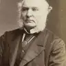 Sepia studio portrait of an elderly man with white mutton-chop whiskers, wearing a dark coat.