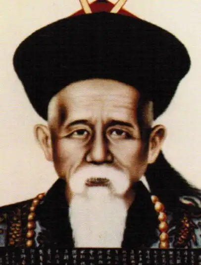 Colour portrait painting of an elderly man with a white beard, wearing a black Qing official hat with a red button and a beaded necklace.