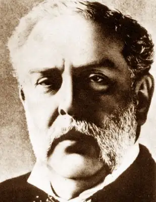 Sepia close portrait of a man with swept hair and a grey beard, in a dark coat.
