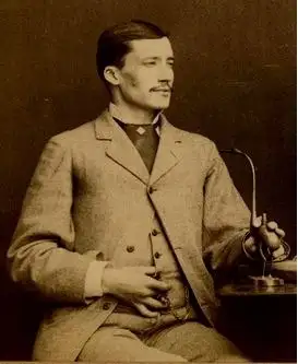 Sepia seated studio portrait of a young man with a moustache in a light suit, looking to the right.