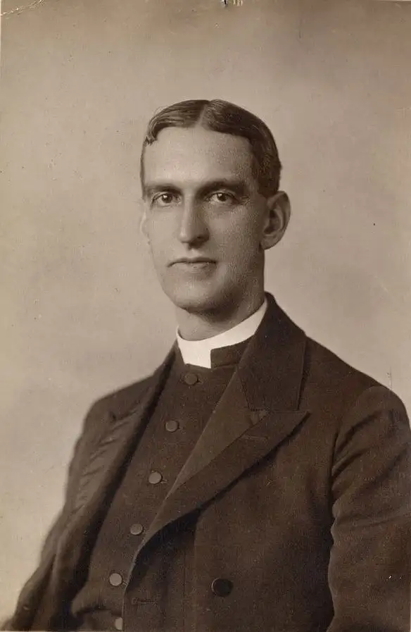 Sepia studio portrait of a clean-shaven man in a dark clerical jacket with a white collar.