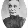 Black-and-white oval portrait of an older man with swept-back hair in a dark mandarin-collar jacket, with a printed name beneath.