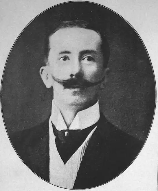 Black-and-white oval portrait of a man with an upturned moustache, in a dark jacket and high white collar.
