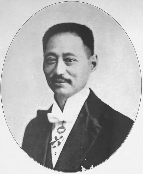 Black-and-white oval portrait of a smiling man with a moustache in evening dress with a white bow tie and a decoration.