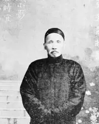 Black-and-white full-length photograph of an older man in a long dark gown standing on garden steps, with Chinese calligraphy written over the picture.