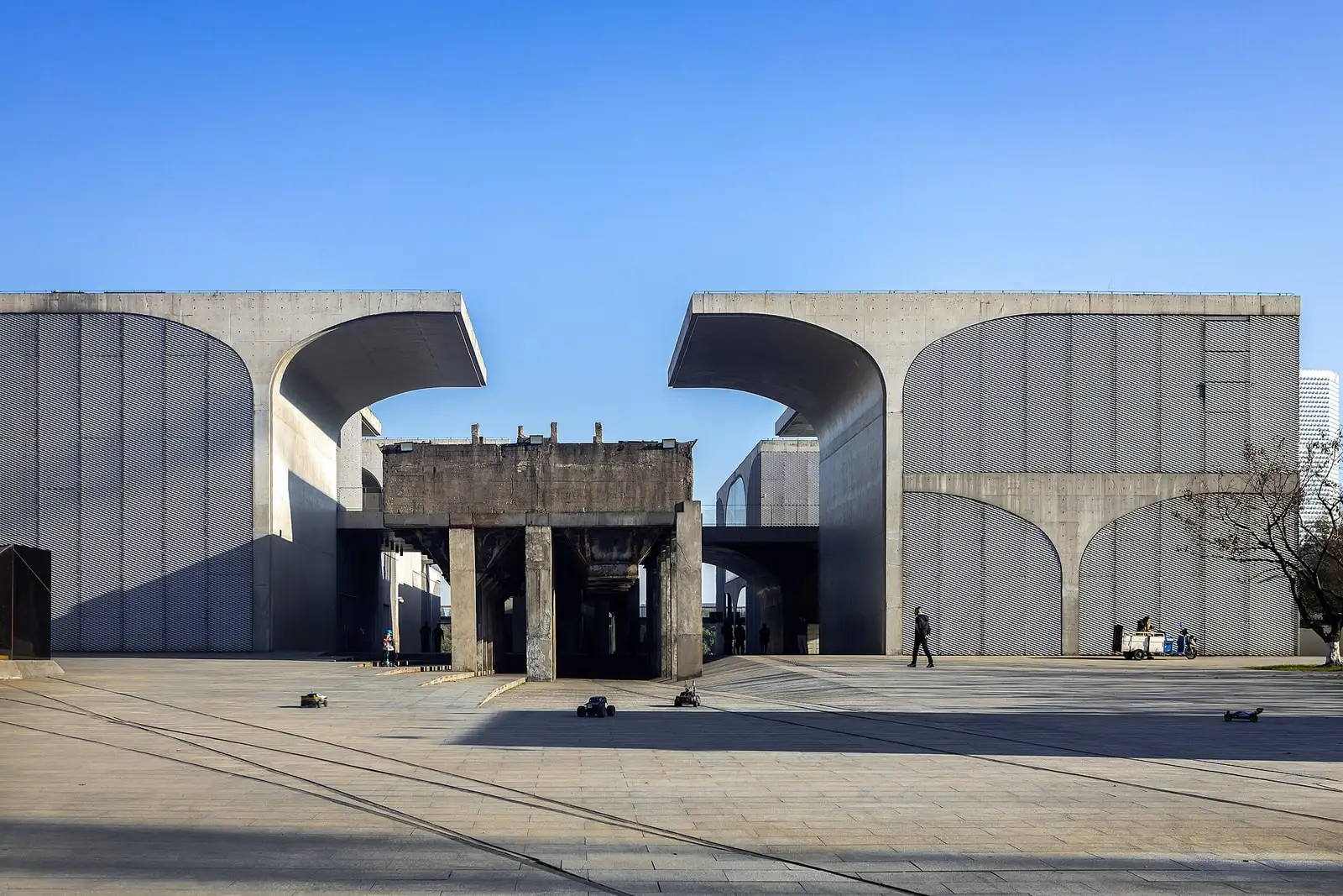 The concrete vaults of Long Museum West Bund framing a brick structure and a paved forecourt.