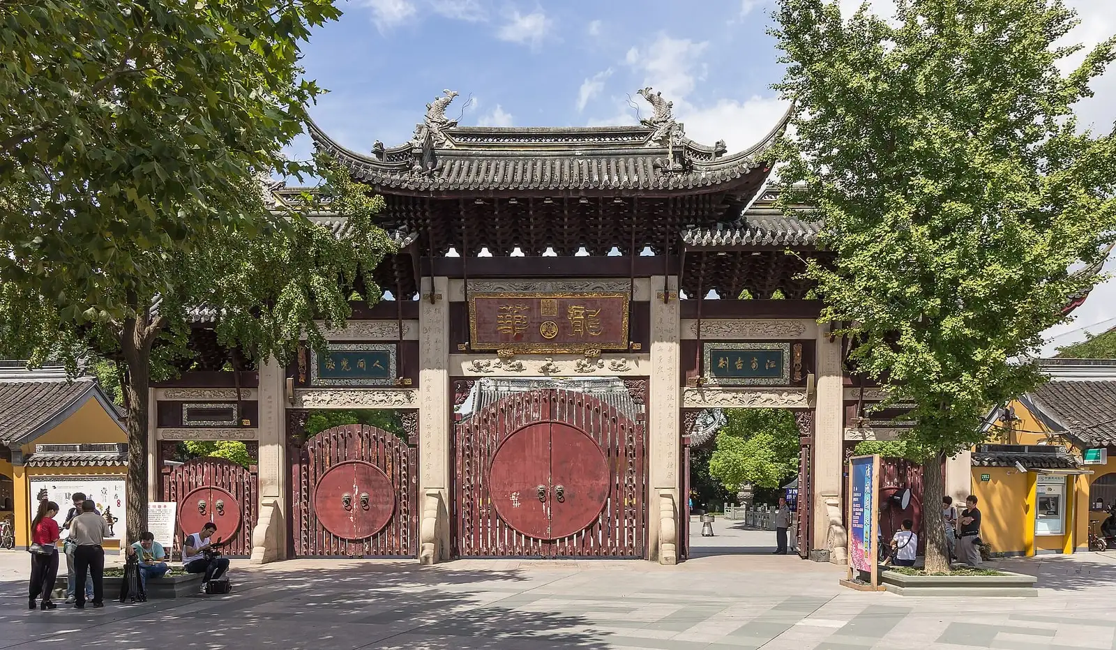 The entrance gate of Longhua Temple, with grey tiled eaves, a circular red door and stone lions.