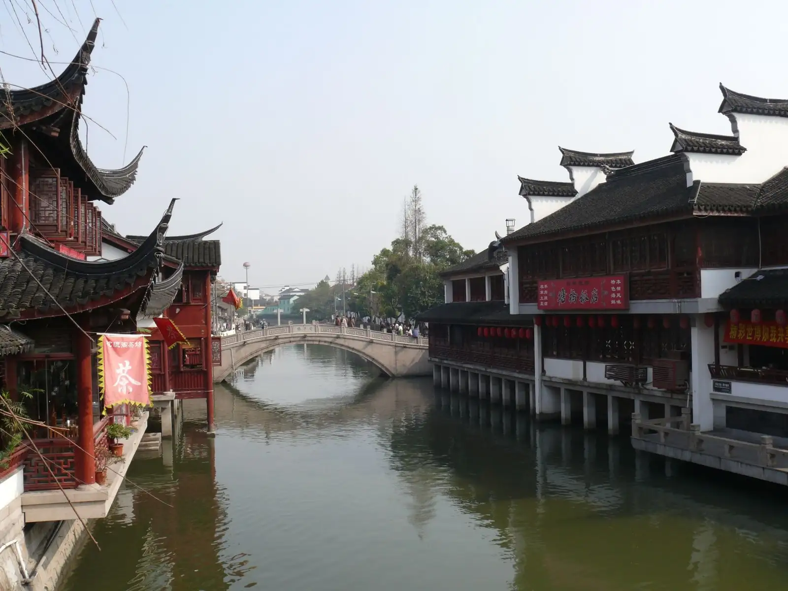 A canal in Qibao Old Town, lined with white-walled buildings and crossed by a stone bridge.