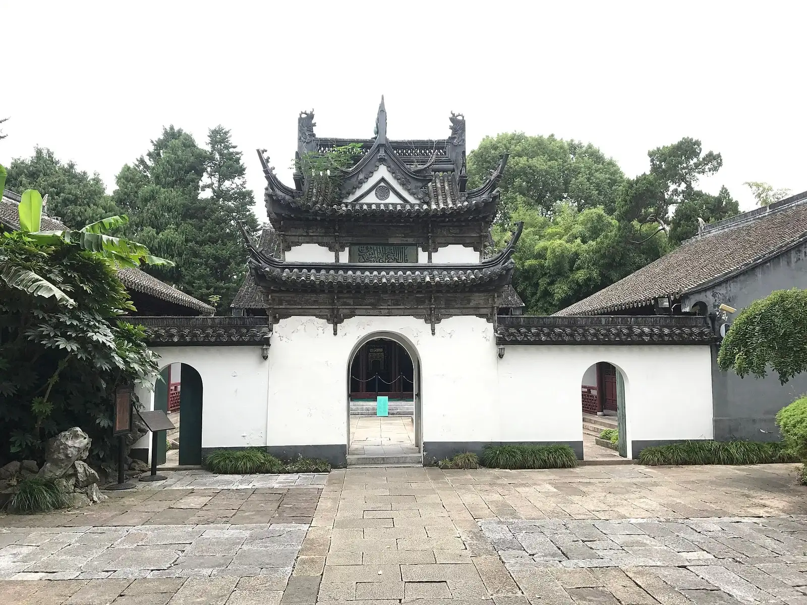 The white courtyard gateway of Songjiang Mosque, with a small tiled pavilion above its arched doorway.