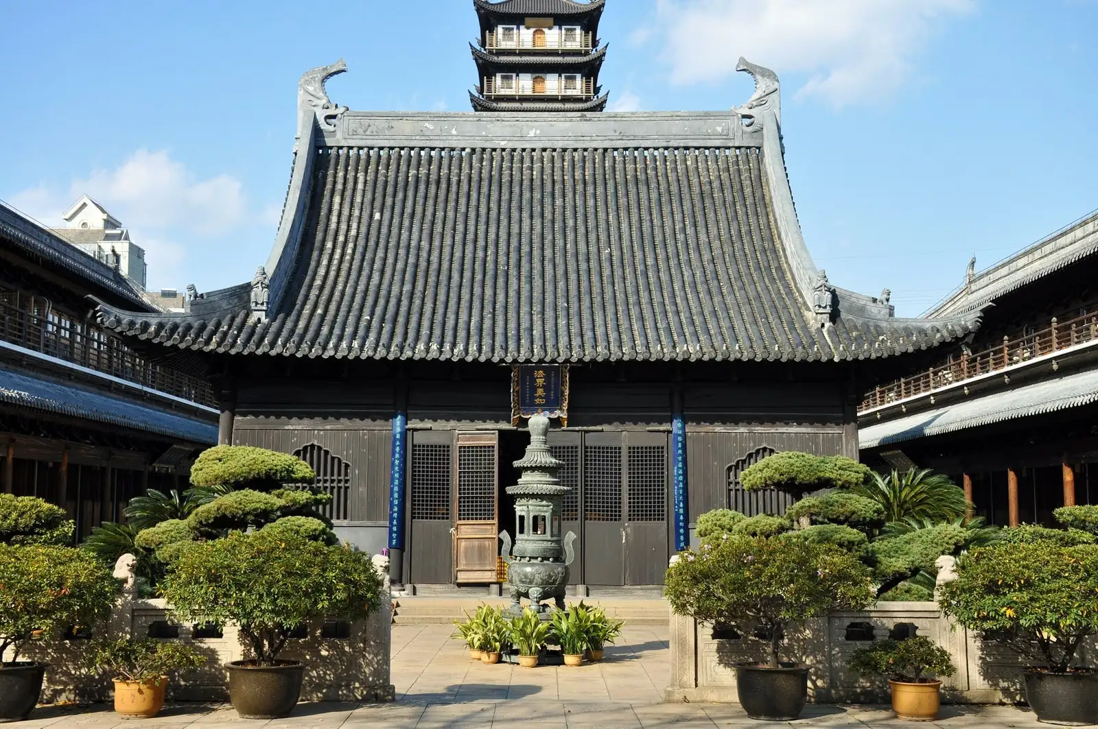 The main hall at Zhenru Temple, framed by potted trees and stone paving in its courtyard.