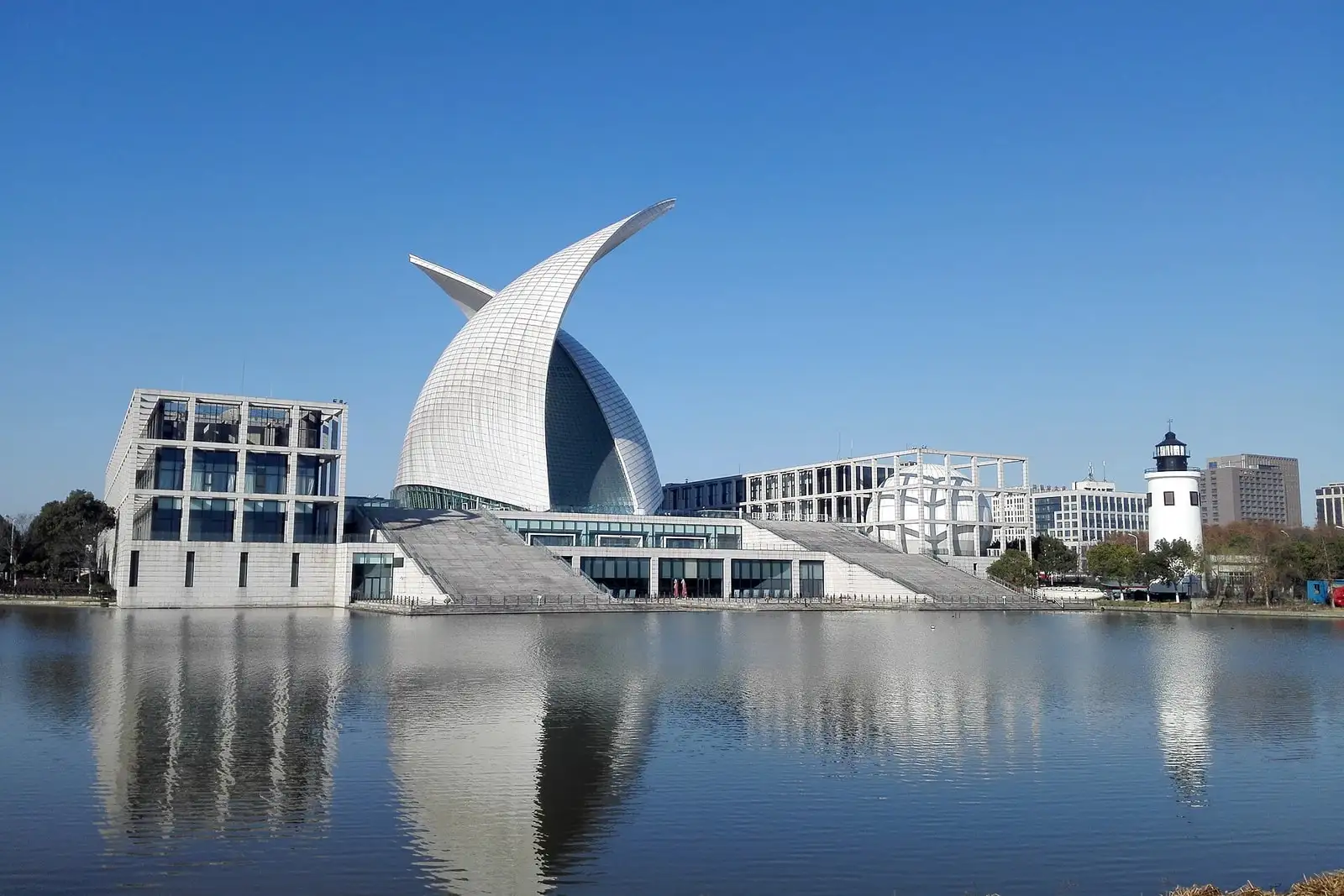 The sail-shaped roof of China Maritime Museum reflected in a pool beneath a blue sky.